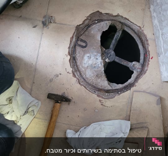 פתח ביוב פתוח עם פטיש ומברג על הרצפה